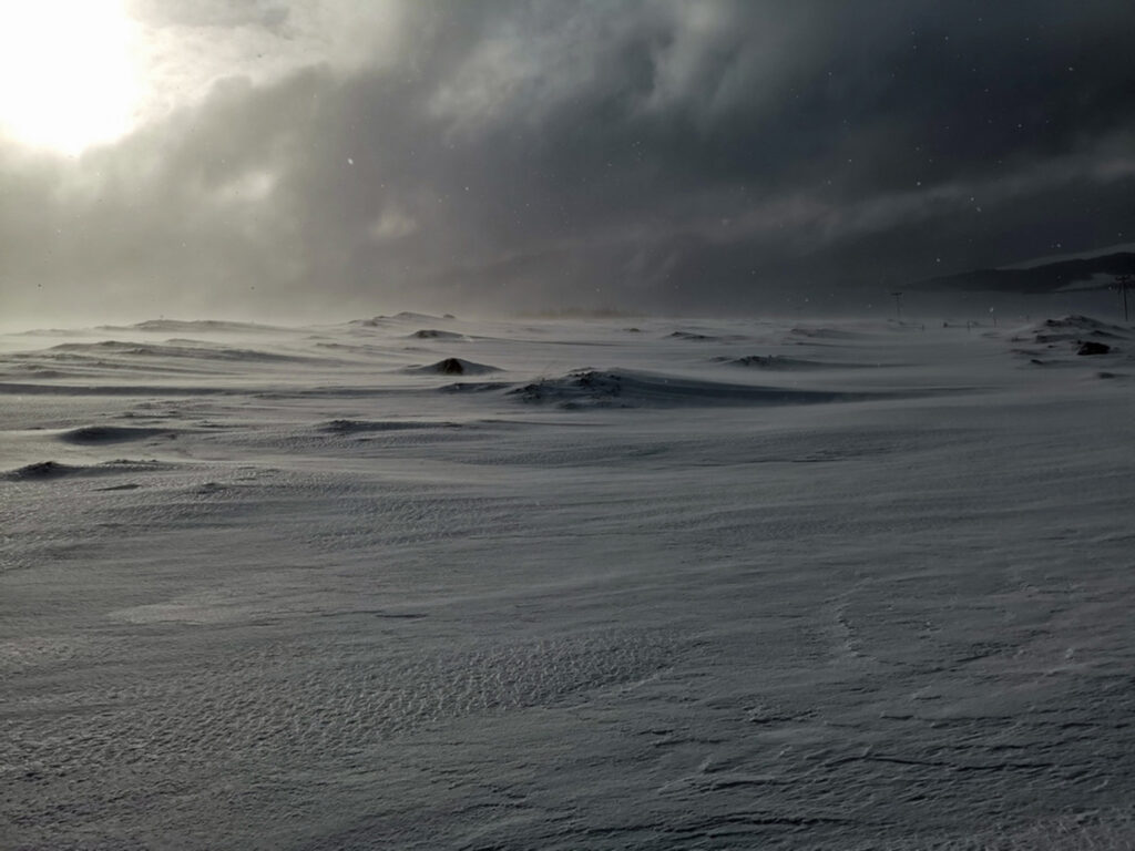 A short winter's tale about remote living  a photograph of a remote, snow covered landscape with clouds of snow coming in and blocking the light